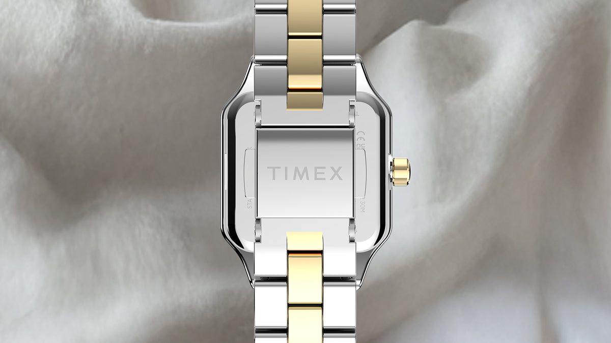 Vista trasera del reloj Timex Addison, en la que se aprecia su caja en tono plateado, su brazalete bicolor y el cierre grabado con el logotipo de Timex.