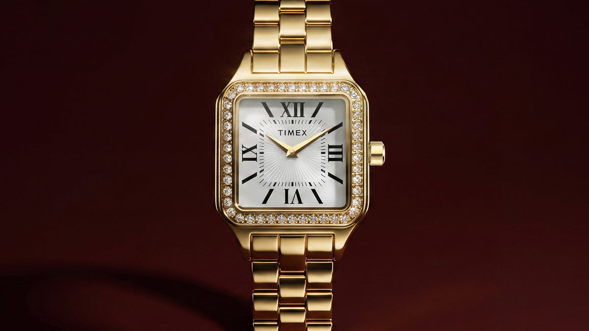 TW2Y90500 Close-up of the gold-tone Timex Addison watch, showing its white textured dial, black Roman numerals, gold-tone hands, and crystal-lined bezel.