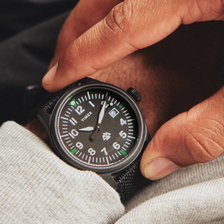 Expedition North Traprock in Black displayed on a man's wrist.  The man is holding both sides of the bezel while he admires the look of this watch and its strap.