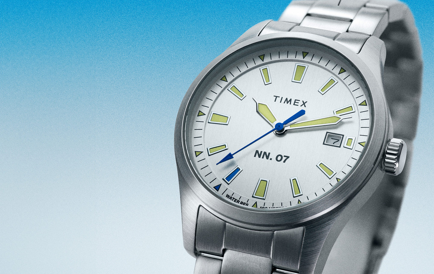 Timex x NN.07 watch displayed with a silver dial and intricate details such as a blue sweep.  The watch is angled on a blue and white ombre background.