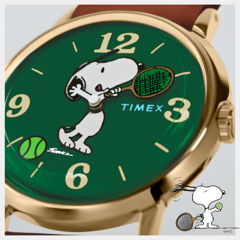 Close-up of the Peanuts x Timex Marlin Hand-Wound watch featuring Snoopy playing tennis on a green dial with a gold-tone case and brown leather strap.
