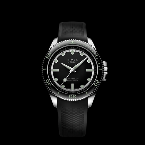 Product display of the Timex Atelier GMT Automatic with a black rubber strap, featuring luminous hour markers and orange GMT hand.