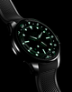 Nighttime image of the Timex Atelier GMT Automatic glowing in green lume, showing its legibility in low light.
