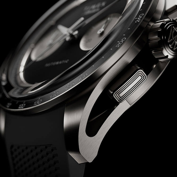 Detailed macro shot of the Timex Atelier Chronograph Automatic M1A Ti featuring a brushed titanium case, tachymeter bezel, signature crown, chronograph pusher, and precision-crafted lug design.
