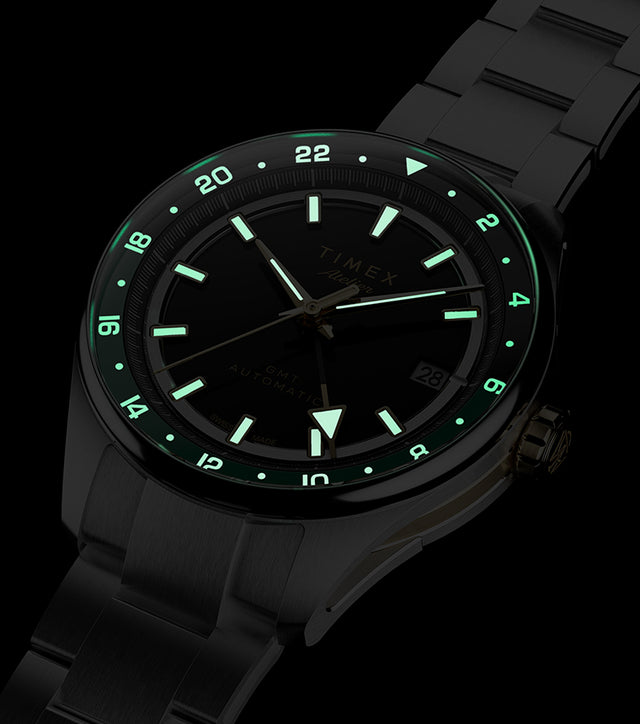 Reloj Timex Atelier GMT Première M1a que brilla en la oscuridad, con índices horarios, agujas y escala de 24 horas iluminados.