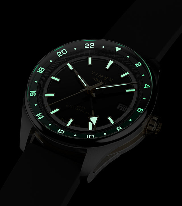 Timex Atelier GMT Première M1a watch glowing in the dark with illuminated hands, hour markers, and 24-hour scale.