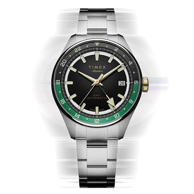 Vista frontal del reloj Timex Atelier GMT Première M1a, con esfera negra, escala GMT verde y brazalete de acero inoxidable.