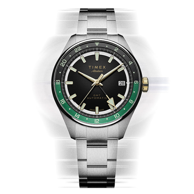 Vista frontal del reloj Timex Atelier GMT Première M1a, con esfera negra, escala GMT verde y brazalete de acero inoxidable.