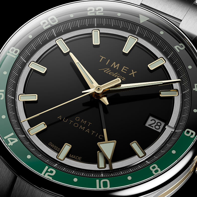 Primer plano de la esfera negra, los índices luminosos en tono dorado, la manecilla GMT, la escala de 24 horas en verde y la ventanilla de la fecha.