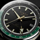 Close-up of the black dial, luminous gold-tone markers, GMT hand, green 24-hour scale, and date window.