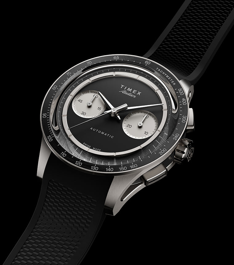 Timex Atelier Chronograph Automatic M1a Ti titanium watch with black dial, silver-tone sub-dials, tachymeter bezel, and textured black rubber strap shown at an angled perspective.