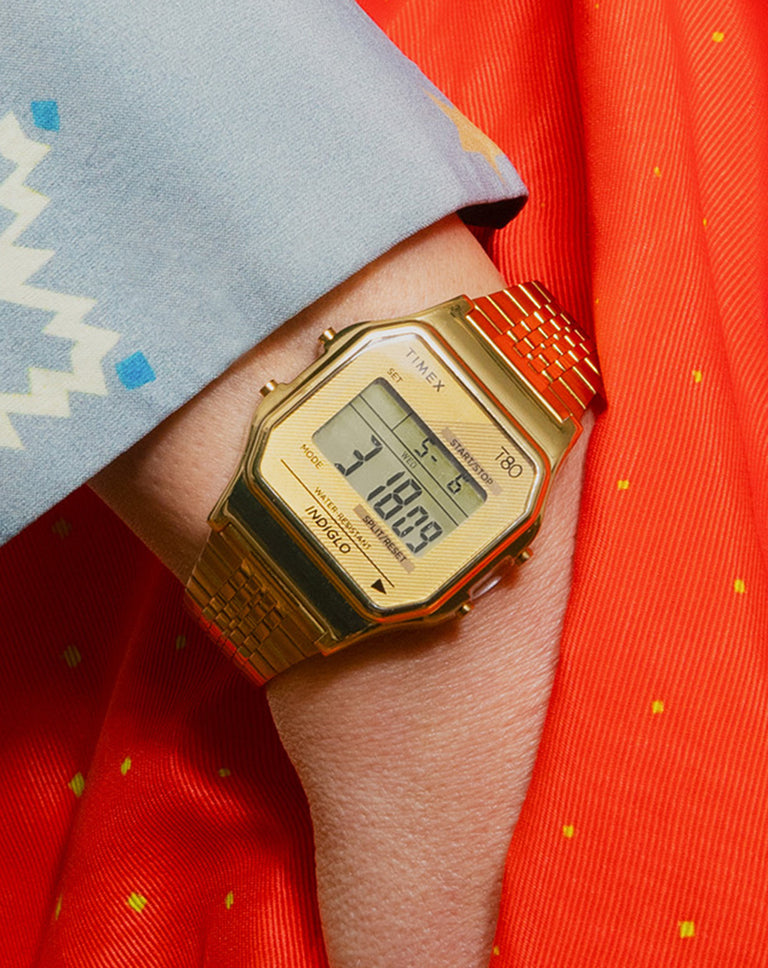 Timex T80 digital watch with gold-tone case, digital display, and metal bracelet worn on wrist.