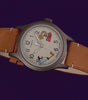 TW2Y99400 Vistas giratorias del reloj Road Runner & Wile E. Coyote x Timex Expedition® Scout, en las que destacan su esfera con motivos de los personajes, la caja gris y la correa de piel marrón sobre fondos morados y rojos.