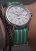 A Timex Weekender watch with a white dial and teal-and-white striped fabric strap, rotating and displayed in different angles to highlight its design features, including the black numerals, date window, silver-tone case, and Indiglo backlight.