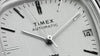 Video showcasing the Timex® Automatic 1983 E Line Reissue watch (model TW2W70800) rotating on a map-themed background with yellow accents. The footage highlights the brushed stainless-steel case and integrated bracelet, silver sunburst dial with minimalist hour markers, and date window at 3 o’clock.