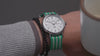 A Timex Weekender watch with a white dial and teal-and-white striped fabric strap, rotating and displayed in different angles to highlight its design features, including the black numerals, date window, silver-tone case, and Indiglo backlight.