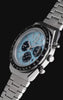 Q Timex Chronograph watch rotating against a black background, showcasing its light blue dial, black chronograph subdials, tachymeter bezel, and stainless-steel bracelet.