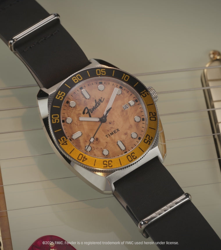 Fender x Timex Automatic watch with a wood-grain dial, black strap, and exhibition case back displayed alongside Fender guitars.
