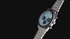 Rotating views of the ice-blue Q Timex Chronograph and its stainless-steel bracelet against a black background.
