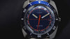 A dynamic video showcasing the Q Timex® 1971 Velocity watch, featuring close-up shots of its blue dial, orange accents, and stainless steel bracelet. The video highlights its retro 1970s racing-inspired design, bold color palette, and precision craftsmanship with smooth camera motion and reflections on a red surface.