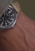 Person wearing the MK1® Automatic watch while handling binoculars, followed by close-up views of its black dial, silver-tone case, and tan fabric strap.
