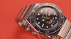 TW2Y99200 Rotating views of the Bugs Bunny x Timex M79 Automatic Signature Edition watch, highlighting its black character dial, carrot-shaped seconds hand, and silver-tone bracelet against red backgrounds.