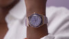 A rotating showcase of the Q Timex® in rose gold-tone with a lilac dial and blue bezel. The watch glimmers under soft light as the camera pans across its details, highlighting the day-date window, luminous markers, and two-tone bracelet with white center links.