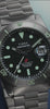 Promotional video featuring the Timex Deepwater Reef 200 Titanium dive watch. The watch is shown in close-up shots highlighting the black dial, aqua luminescent markers, titanium bracelet, rotating bezel, and screw-down crown. Water splashes around the watch, emphasizing its 200-meter water resistance. The lume glows vividly in dark conditions.